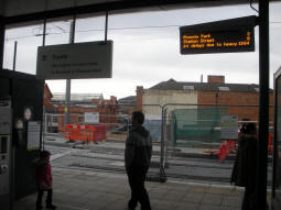 The only display at the platform level faces into the sheltered area at the top of the lift and stairs. Building work for the phase two extension continues behind. Platforms are off to the right, access to the railway station footbridge to the left